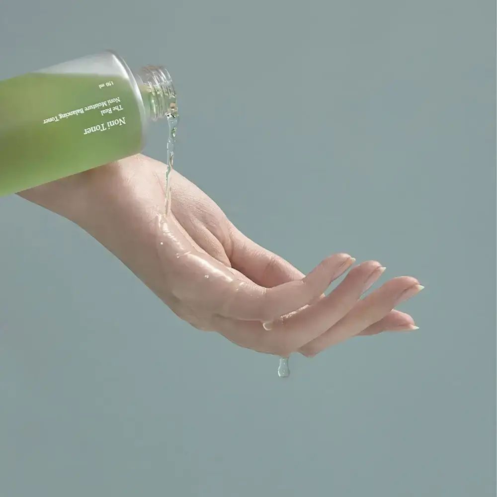 Hand, die Flüssigkeit aus einer Flasche empfängt. Flüssigkeit ist klar und grünlich. Hintergrund blau.