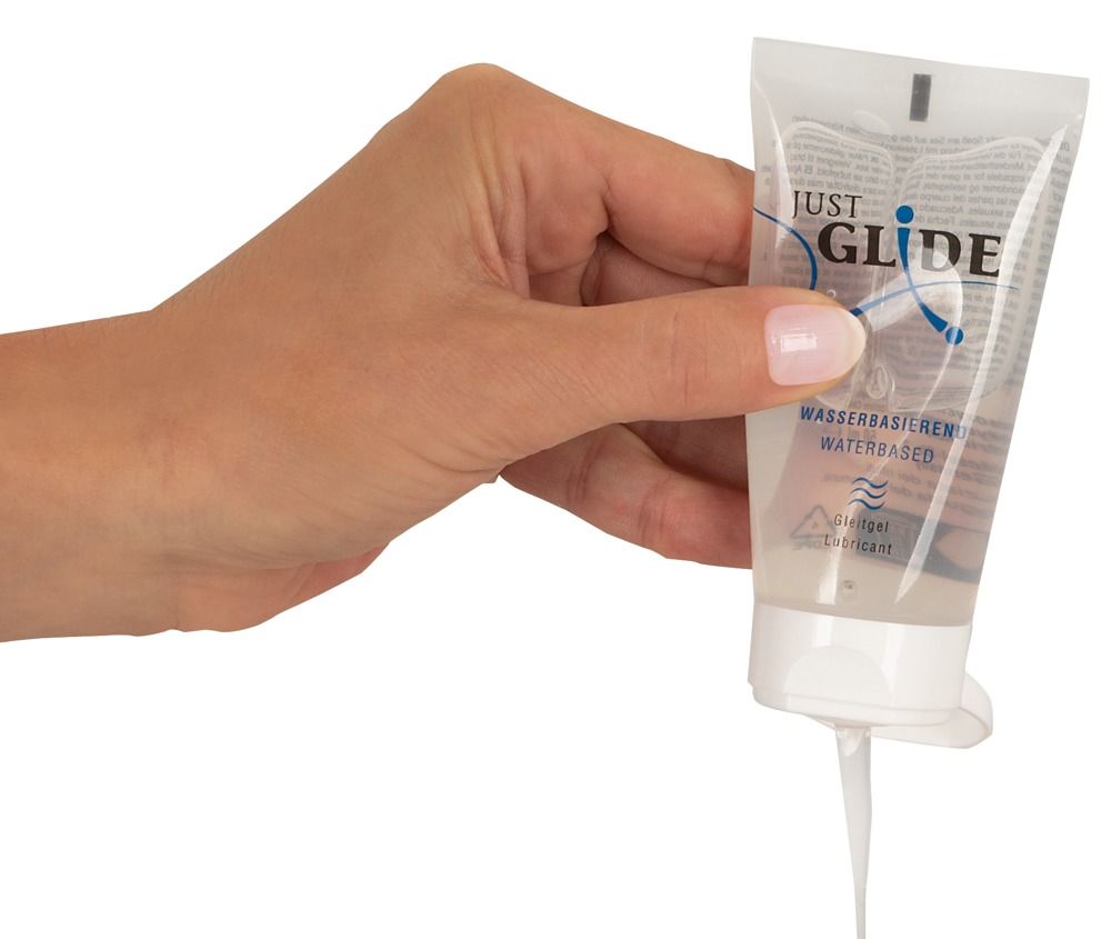 Hand hält Tube. Produktname: JUST GLIDE. Aufschrift: Wasserbasiert, Gleitgel/Lubricant. Gel fließt aus der Öffnung.