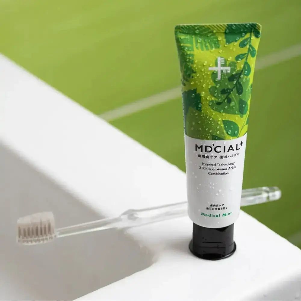 Zahncreme-Tube MD'CIAL+ neben Zahnbürste. Grünes Design, Schriftzug Medical Mint. Schwarzer Verschluss.