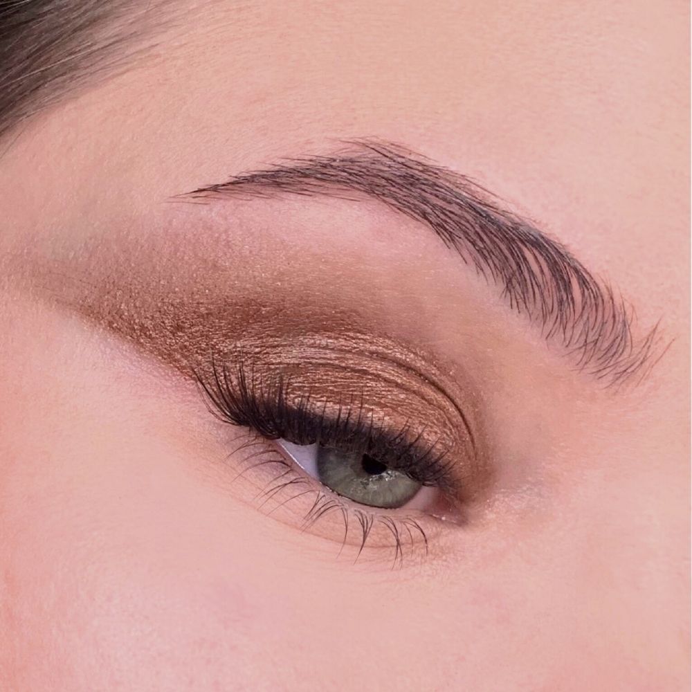 Auge mit goldbraunem Lidschatten. Lidschatten auf dem Augenlid und als Lidstrich aufgetragen. Braune Augenbraue.