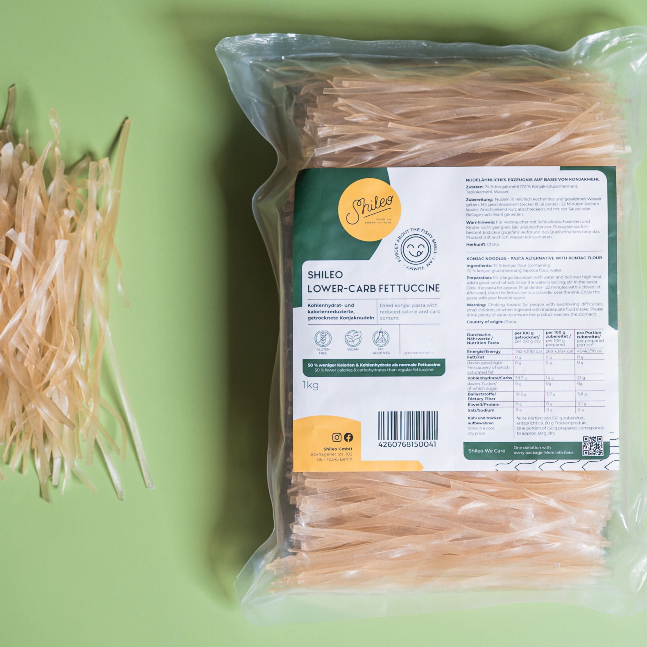 SHILEO Lower-Carb Fettuccine in Verpackung. Klare Plastikverpackung. Einige Nudeln liegen daneben. Grüner Hintergrund.