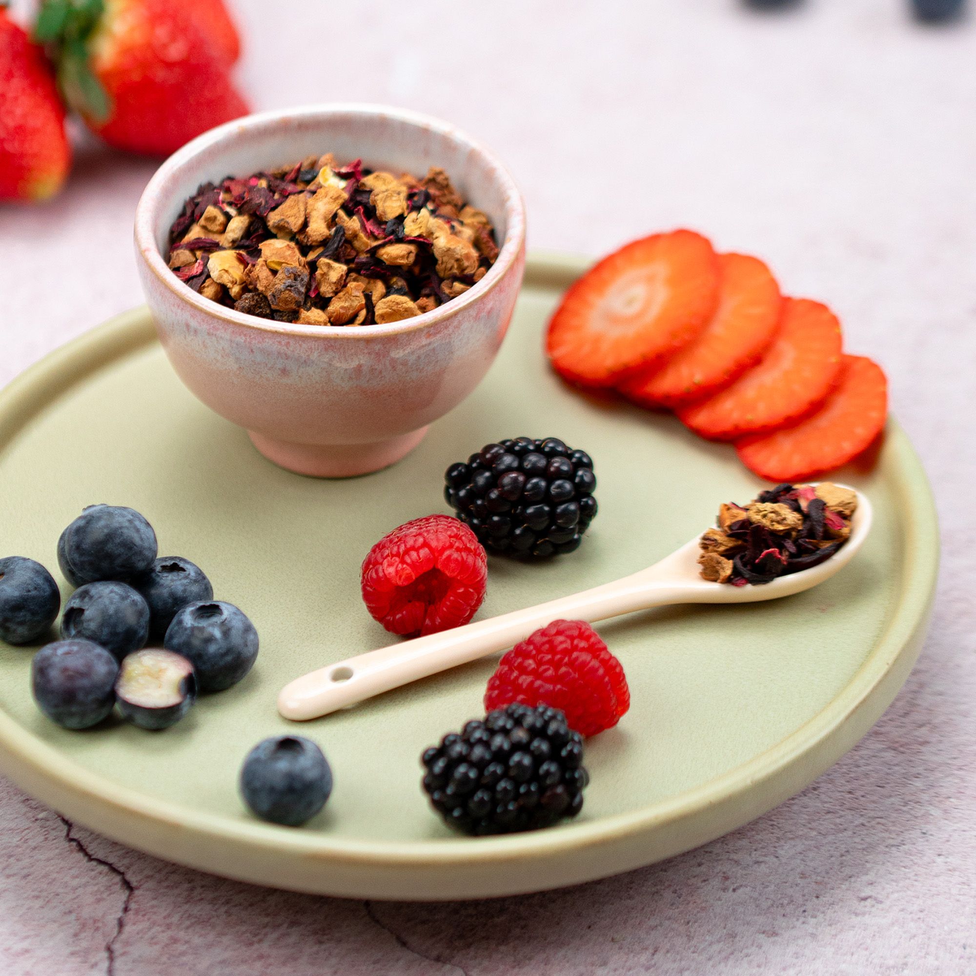Schale mit losem Früchtetee, daneben Beeren und ein Löffel mit Tee. Auf einem Teller liegen Beeren und Früchte.