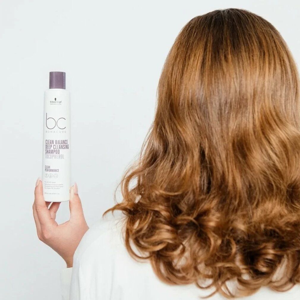 Person hält Shampoo-Flasche. Aufschrift: BC Bonacure Clean Balance Deep Cleansing Shampoo. Lange, gewellte Haare.