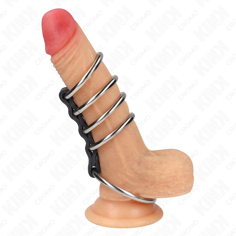 Penisring mit vier Ringen aus Metall, verbunden mit einem schwarzen Band. Ein Dildo ist in den Ring eingesetzt.