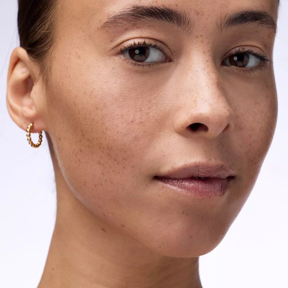 Nahaufnahme eines Gesichts mit Sommersprossen und goldenen Ohrringen.