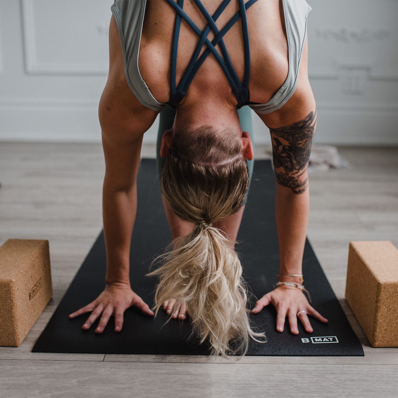 Person in Yoga-Pose auf schwarzer Yogamatte. Zwei Yogablöcke liegen daneben. Logo "B MAT" sichtbar.