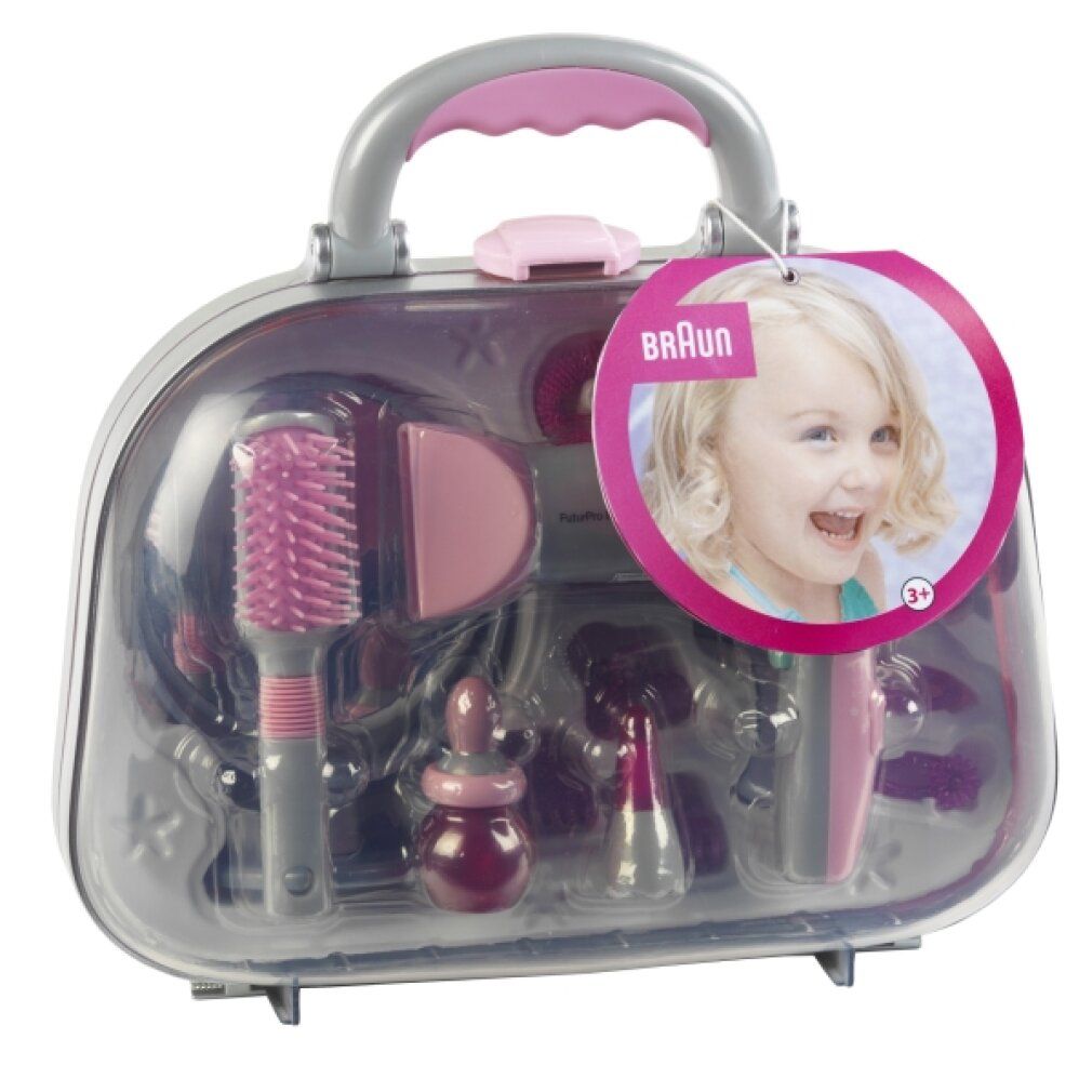 Beauty Case mit Zubehör. Transparente Tasche mit Griff, gefüllt mit rosa und grauen Spielzeug-Accessoires. Braun-Logo.
