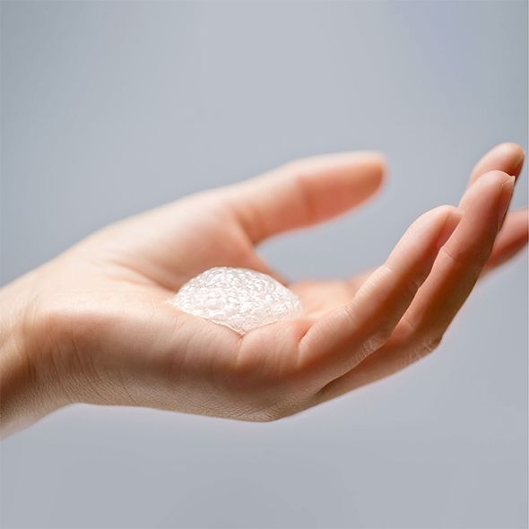 Hand mit einer Kugel aus weißem Schaum. Grauer Hintergrund.