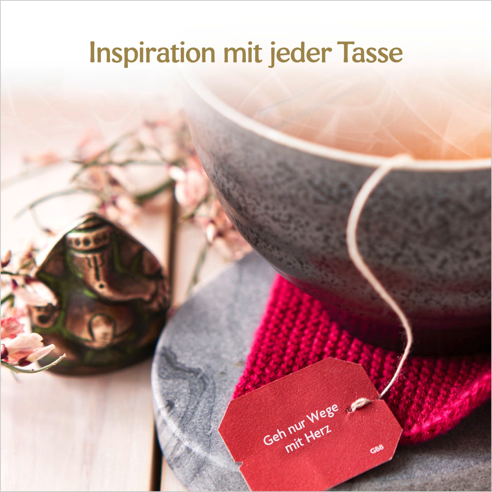 Tasse Tee mit Teebeutel. Rotes Etikett mit Text. Kleiner Buddha. Auf Untersetzer.