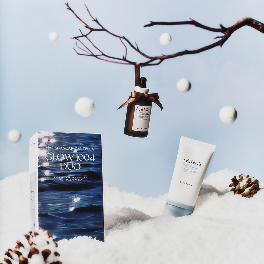 Duo-Set mit Serum, Ampulle und Verpackung. Ampulle hängt an Ast. Serum und Verpackung am Boden. Schneelandschaft.