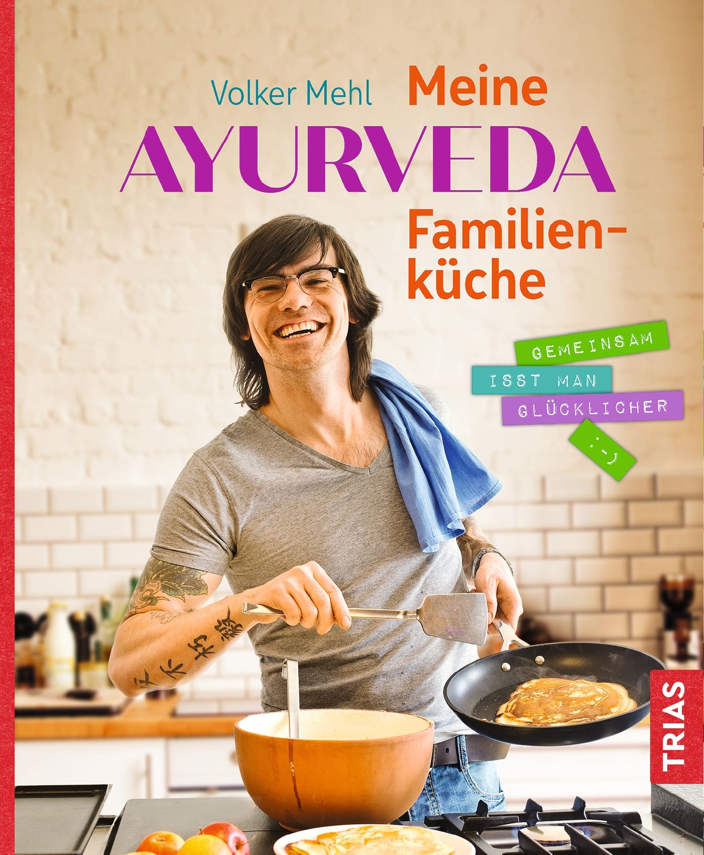 Buchcover: Volker Mehl, Meine Ayurveda-Familienküche. Mann kocht. Titel in Lila und Rot. TRIAS-Logo.