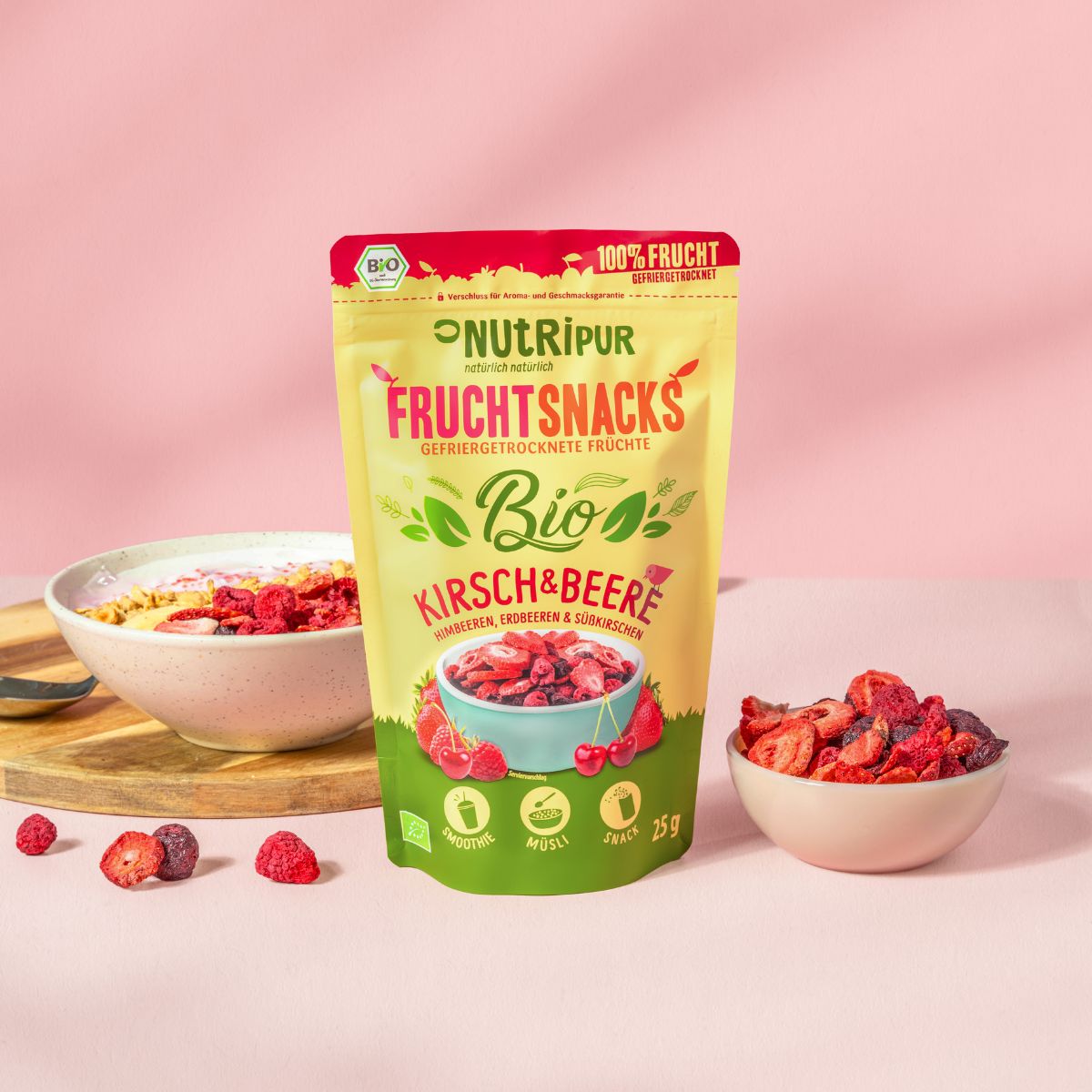Gelbe Tüte "NutriPur Fruchtsnacks Bio Kirsch & Beere". Schale mit Müsli und Früchten. Daneben Schale mit gefriergetrockneten Früchten.