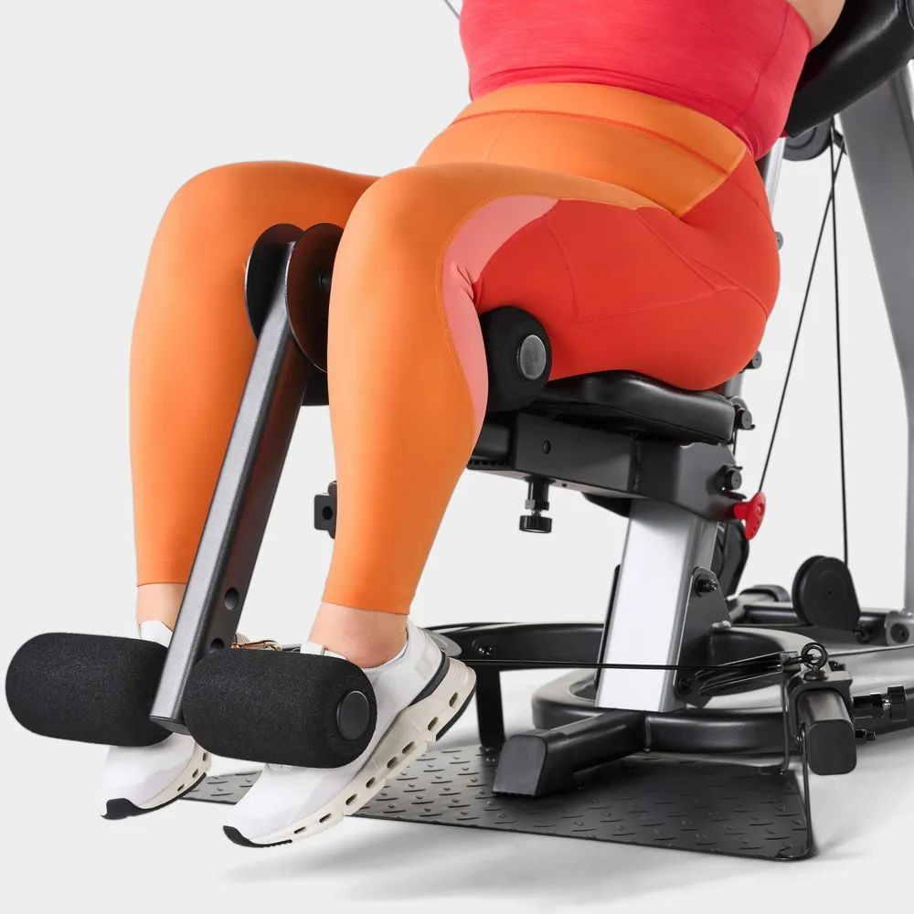 Beine einer Person auf einem Fitnessgerät. Schwarze Polsterung. Orangefarbene Leggings.