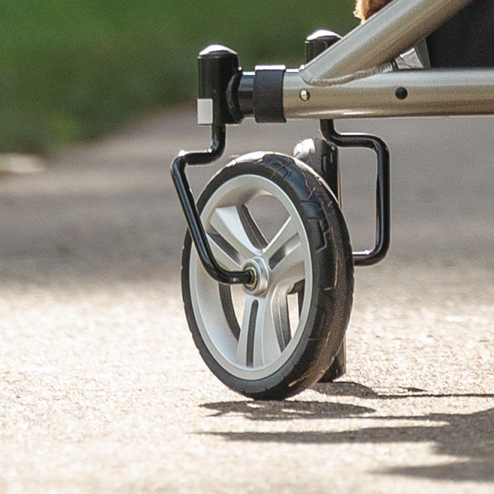 Nahaufnahme eines Rollator-Rades. Graues Rad mit schwarzem Reifen. Der Rahmen ist grau-metallic.