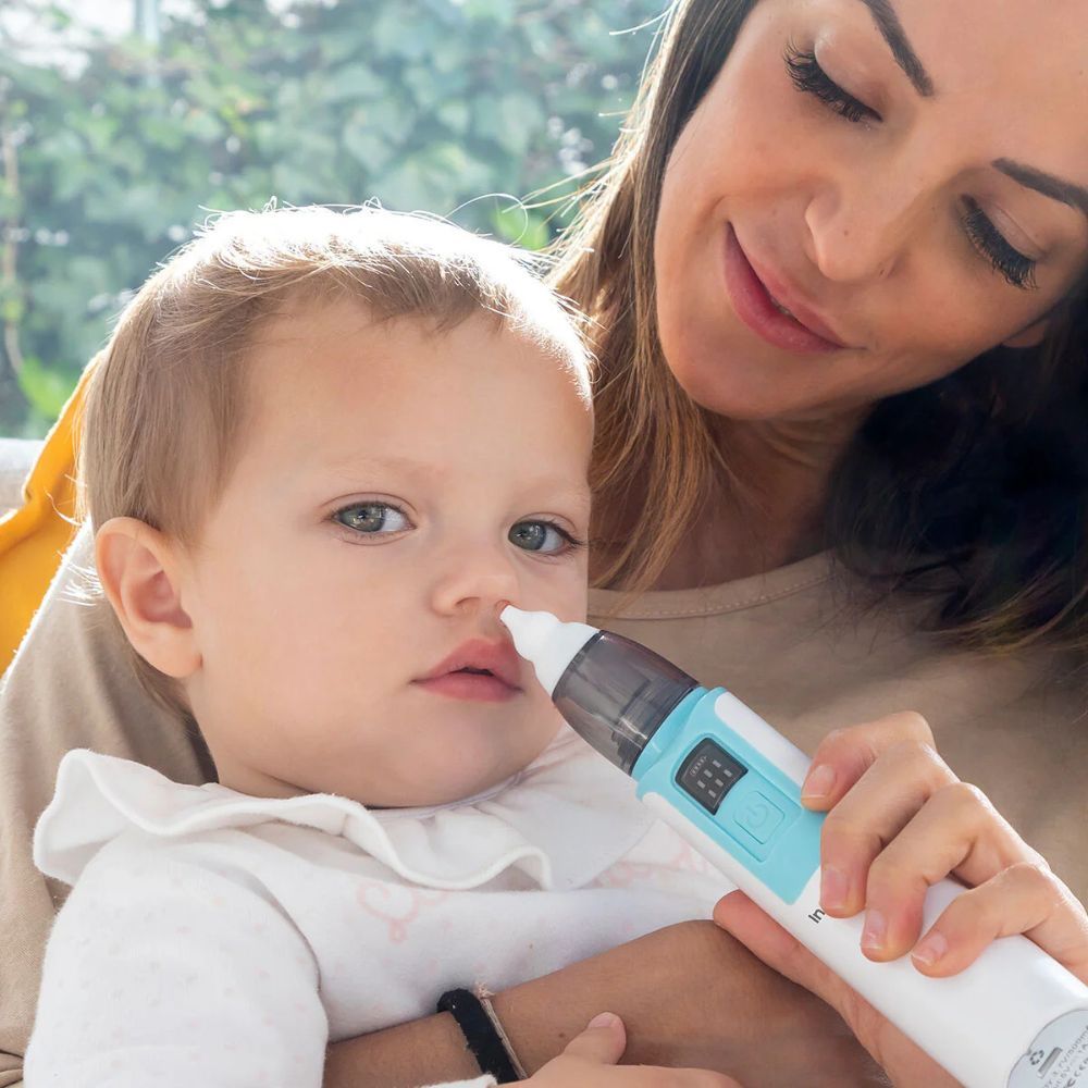 Ein Baby erhält eine Nasenabsaugung. Das Gerät ist weiß und blau. Eine Mutter hält das Baby.