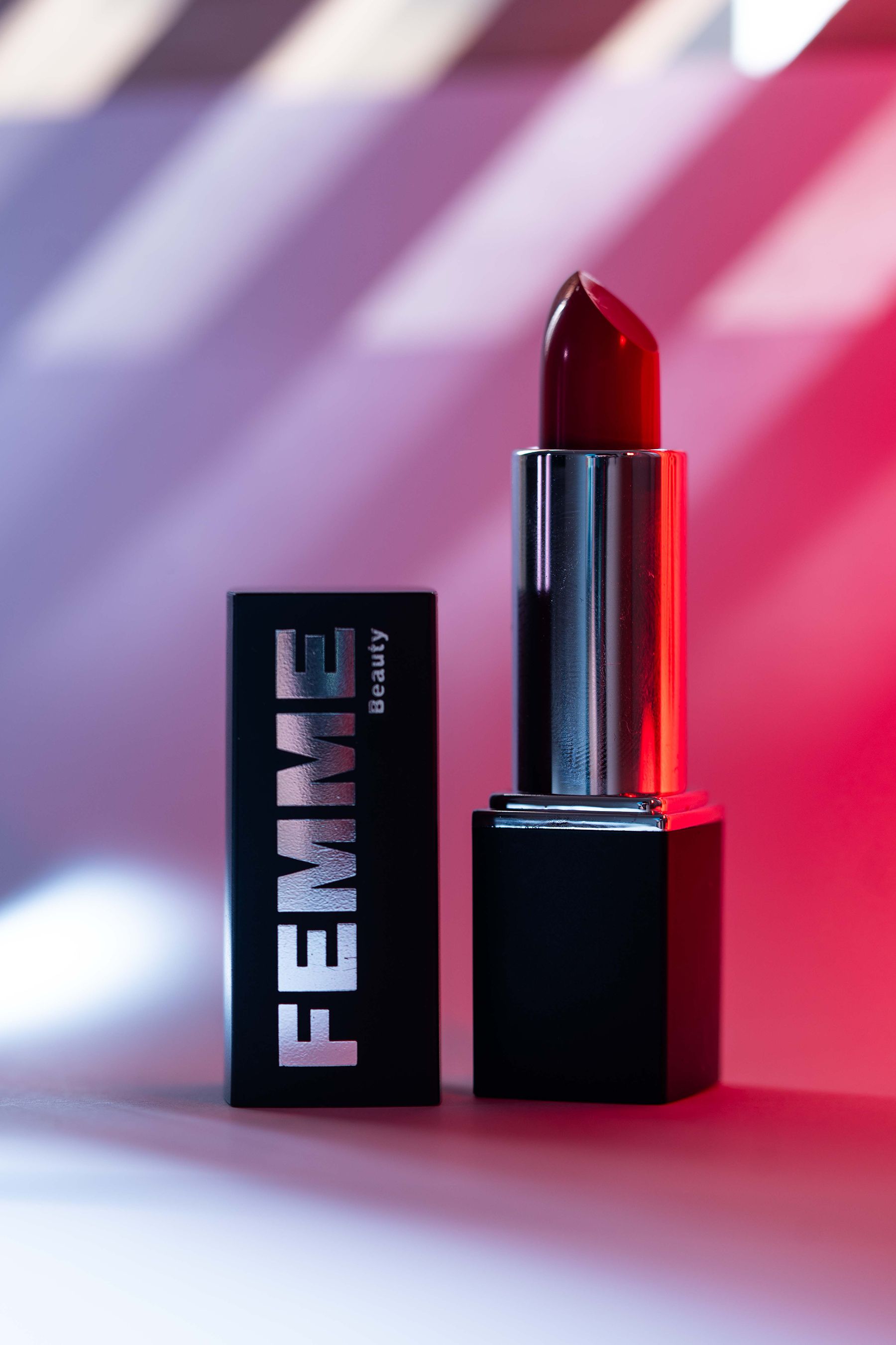 FEMME Visionary Satin Lipstick in Rot, mit abgezogener Kappe, beleuchtet mit rotem und violettem Licht.
