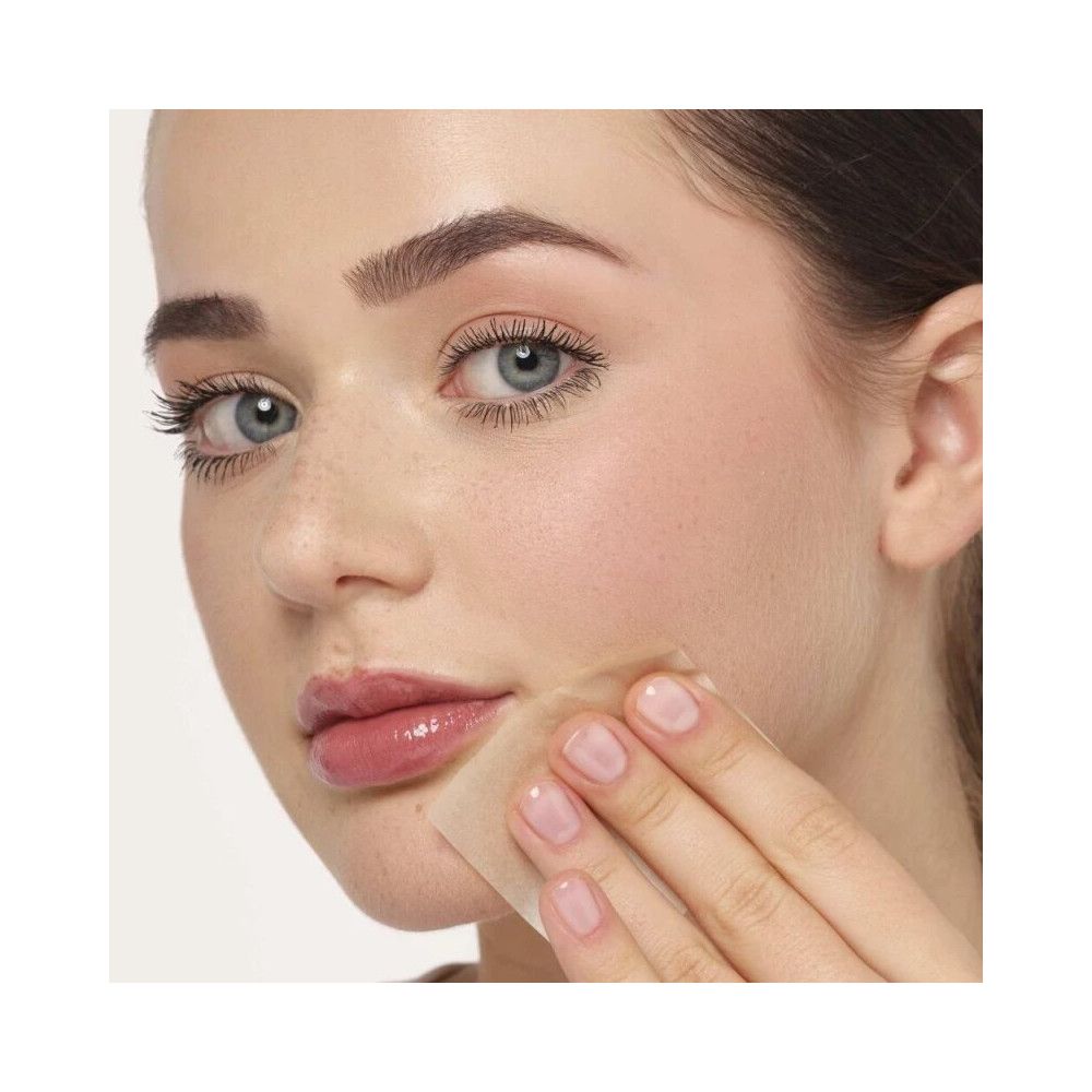 Frau mit Ölpapier, das auf der Haut verwendet wird. Das Papier berührt die Haut, um überschüssiges Öl zu entfernen.