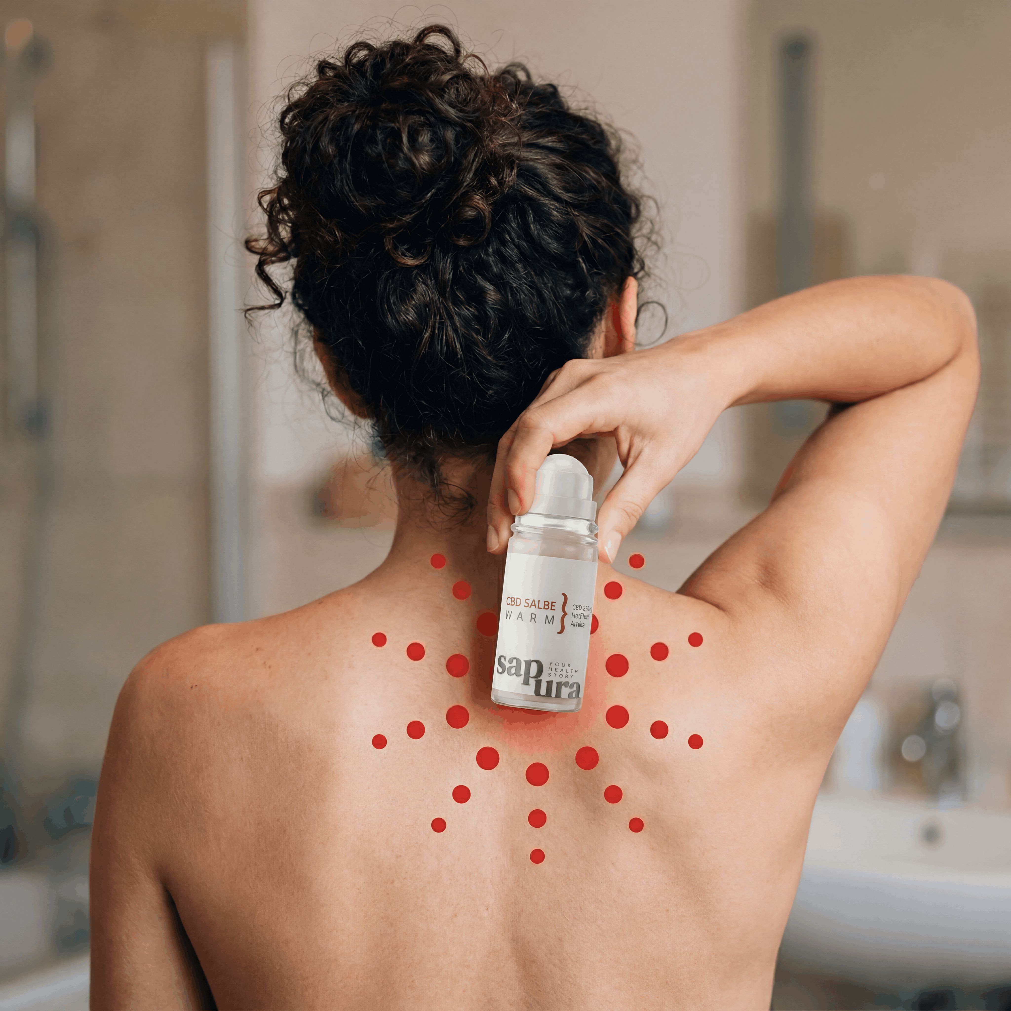 Rückansicht einer Person, die eine CBD Salbe Warm Roll-On Flasche am oberen Rücken hält. Rote Punkte simulieren Wärme.