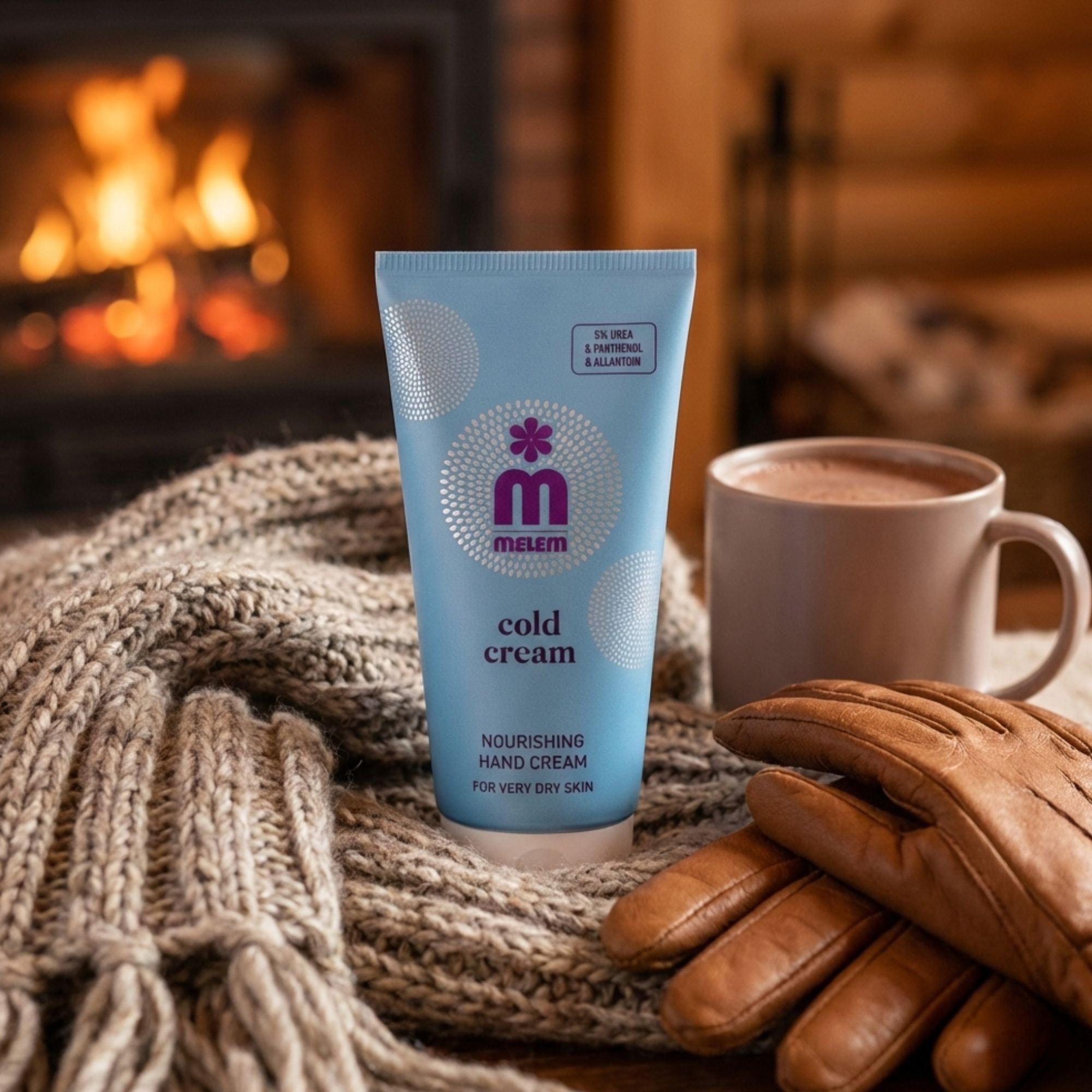 Hellblaue Tube "Melem Cold Cream" auf einem Wollschal. Daneben eine Tasse und Lederhandschuhe. Im Hintergrund Kaminfeuer.
