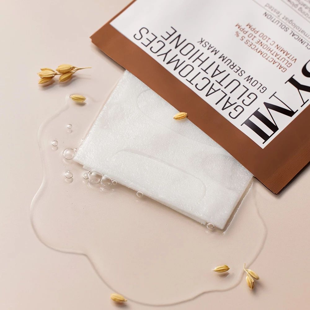 Geöffnete Verpackung mit Serummaske. Daneben Wasser und Getreidekörner. Aufschrift: SOME BY MI, Galactomyces Glutathione Glow Serum Mask.