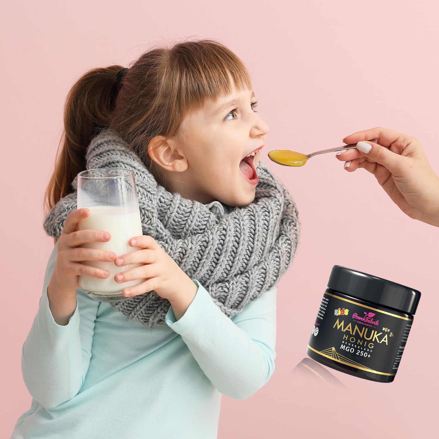 Kind bekommt Honig mit einem Löffel. Auf dem Tisch steht ein Glas Milch und ein Glas Manuka Honig.