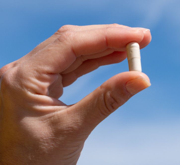 Hand hält eine einzelne Aavalabs Multivitamin Kapsel vor blauem Himmel.