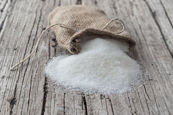 Sack mit weißem, kristallinem Produkt auf Holzuntergrund.