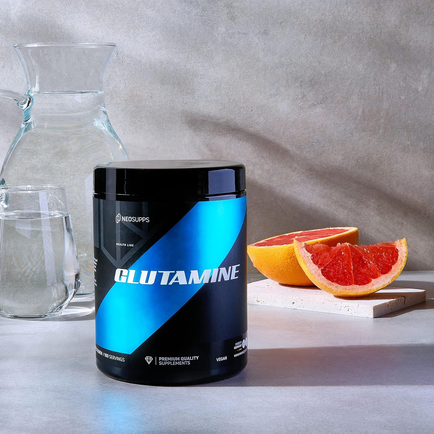 Dunkle Dose Glutamin-Pulver, blaues Design. Neben Wassergläsern und Grapefruit. Text: Glutamine, Premium Quality Supplements.