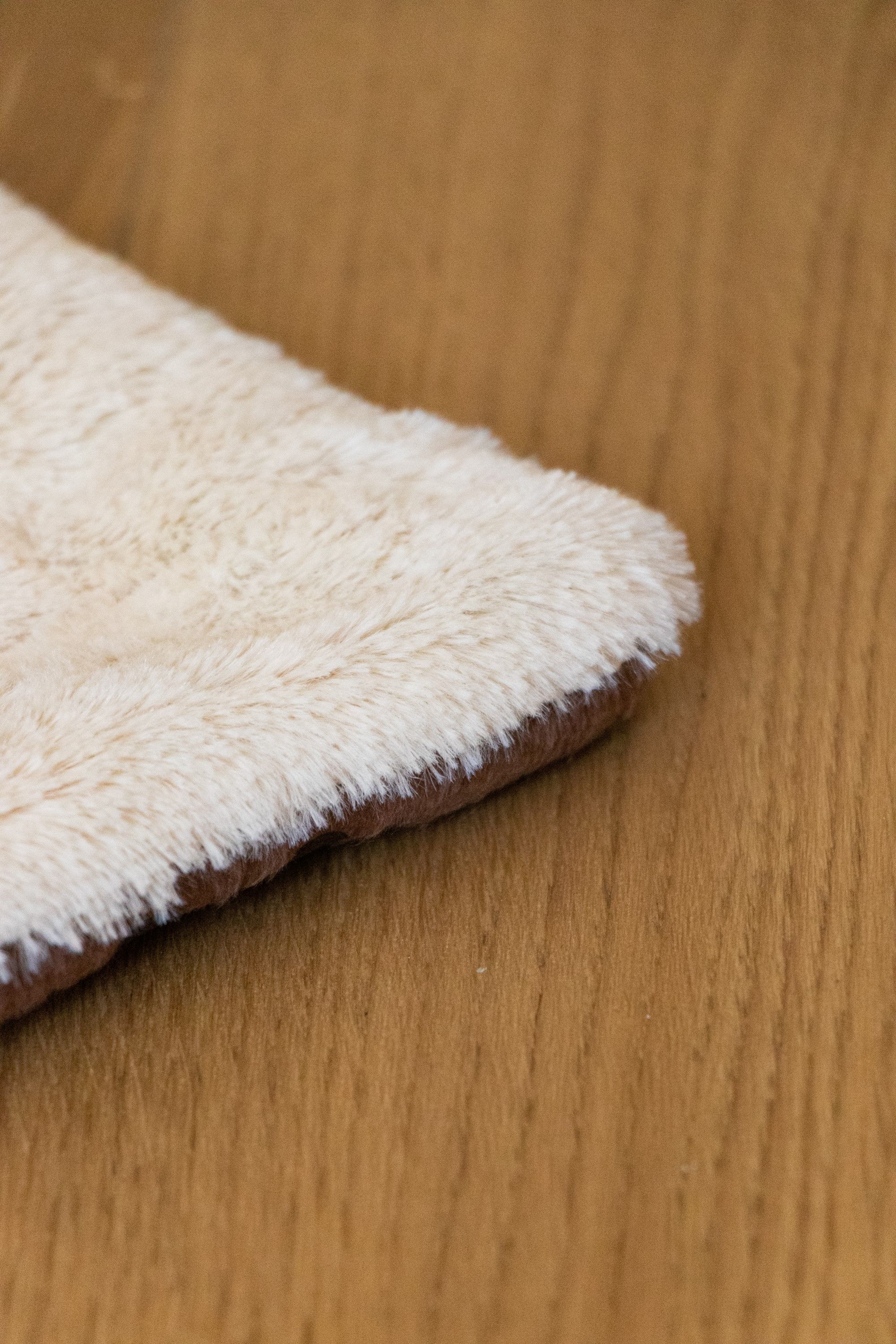 Ausschnitt einer cremefarbenen, flauschigen Decke mit braunem Rand auf Holzuntergrund.