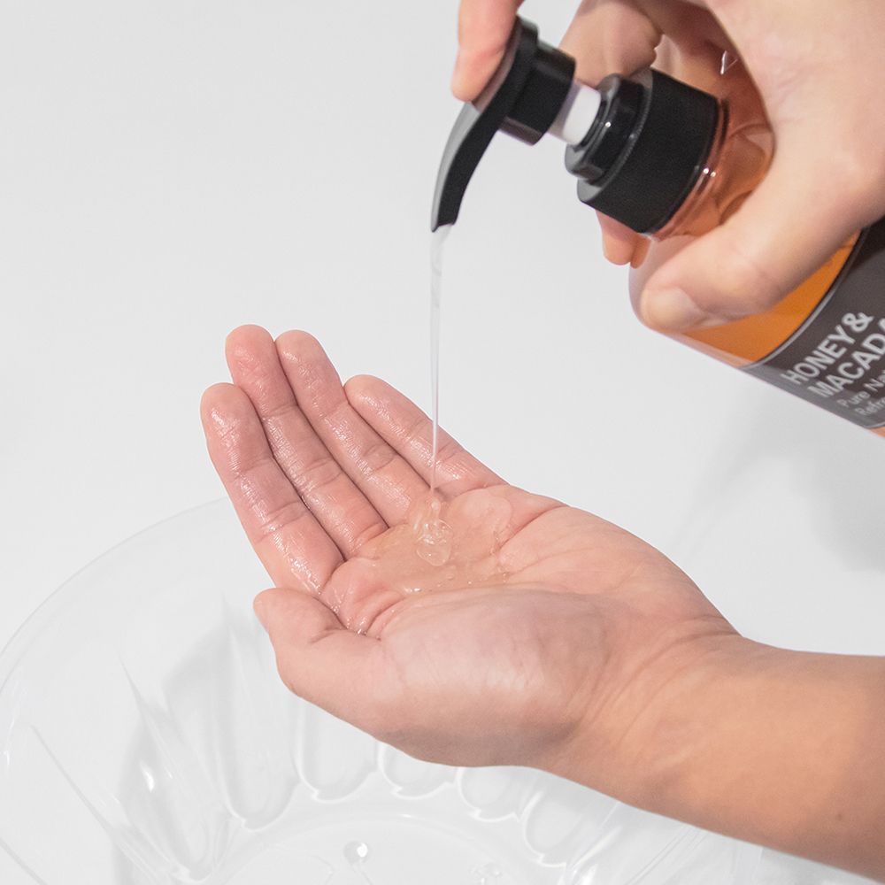 Eine Hand empfängt eine transparente Flüssigkeit aus einer KUNDAL-Flasche. Ein Waschbecken ist im Hintergrund zu sehen.