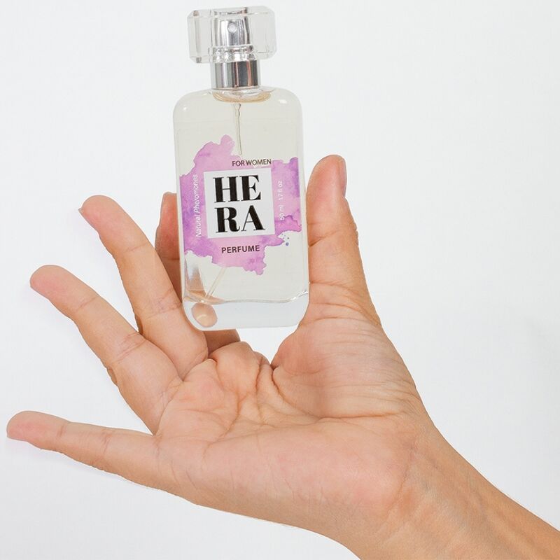 Hera Parfümflasche, transparent, in einer Hand gehalten. Aufdruck mit Text und lila Farbklecks.