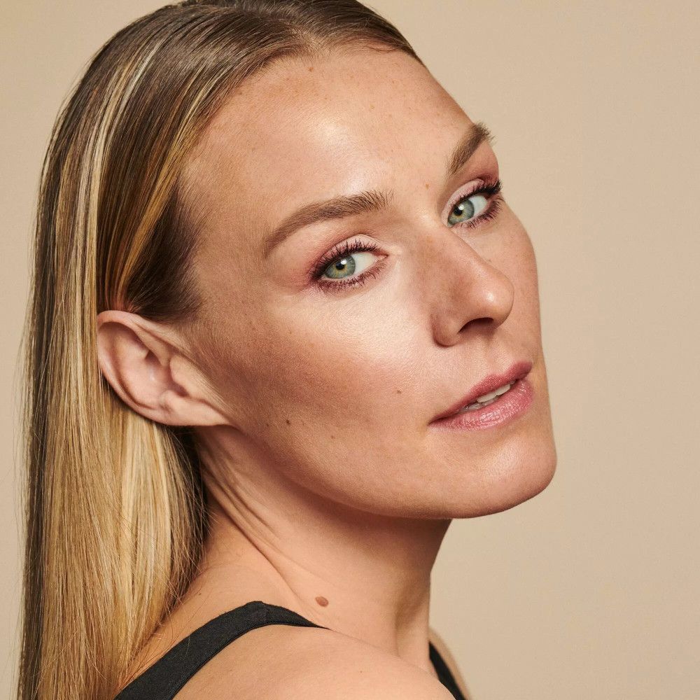 Porträt einer Frau mit blonden Haaren und rosa Lippenstift. Sie schaut in die Kamera.