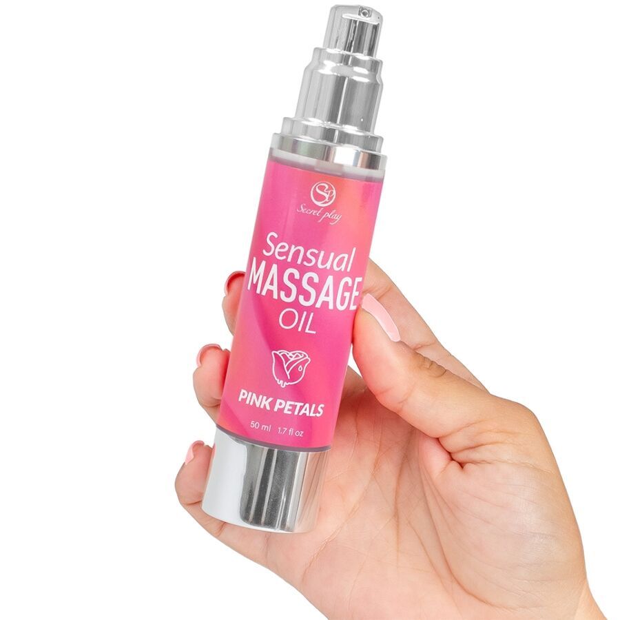 Rosa Flasche mit silbernem Zerstäuber. Aufschrift: Sensual Massage Oil Pink Petals. Wird von einer Hand gehalten.