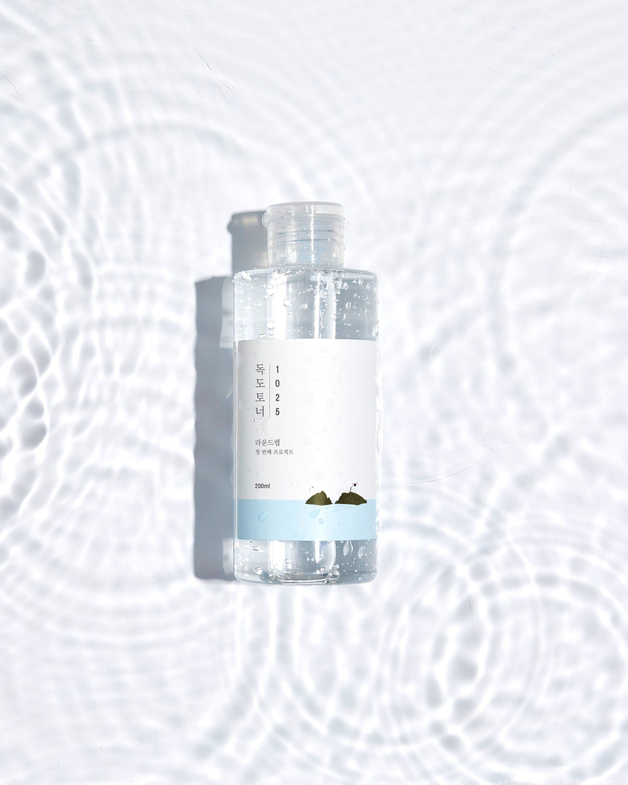 Transparente Flasche mit weißem Etikett. Flasche in Wasser. Wellenmuster. Hellweißer Hintergrund.