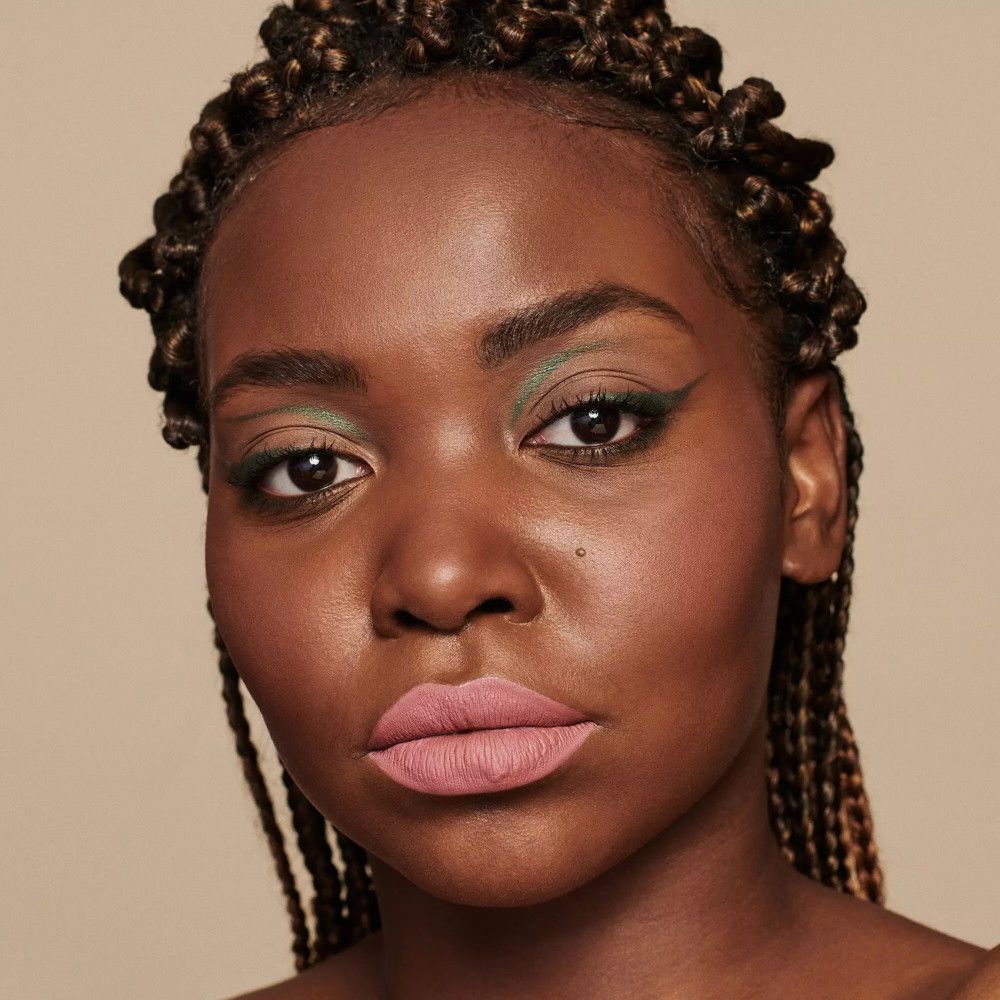 Porträt einer Frau mit geflochtenen Haaren und rosafarbenem Lippenstift. Sie trägt grünen Eyeliner.