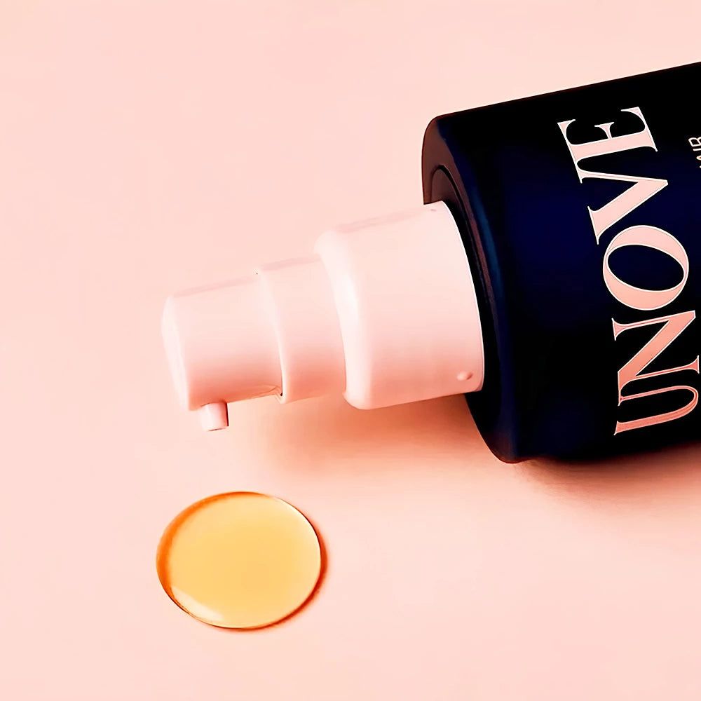 Nahaufnahme des Pumpspenders von UNOVE Silk Hair Oil mit einem Tropfen Öl auf einem rosafarbenen Hintergrund.