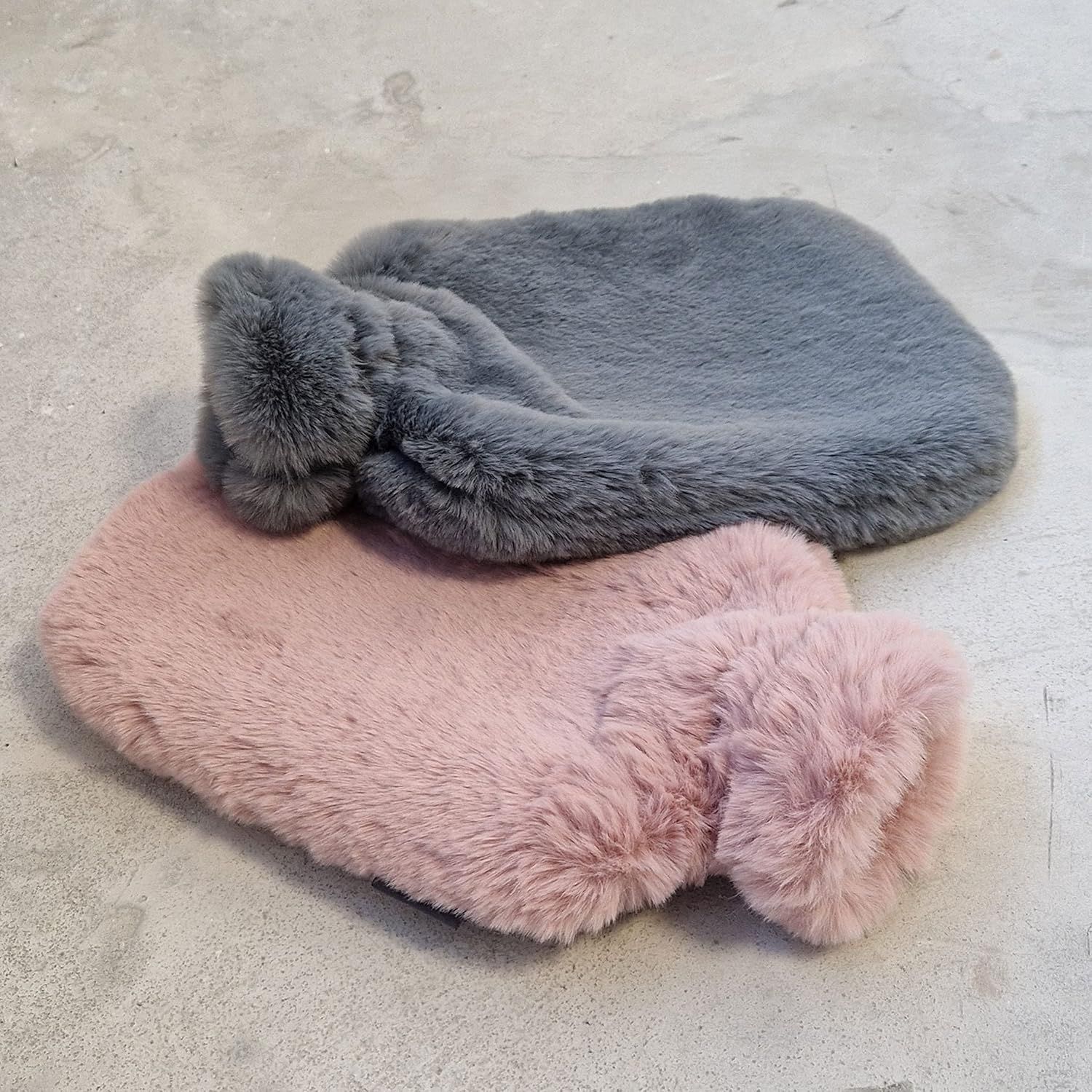 Zwei Wärmflaschen mit flauschigen Bezügen. Grau und rosa. Rechteckige Form mit rundem Hals. Weiches Material.