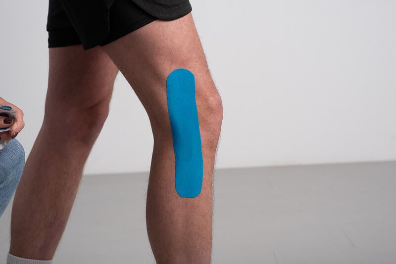 Blaues Kinesiotape auf einem Knie angebracht.