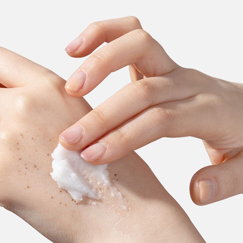 Hand trägt TIRTIR Hydro Boost Enzyme Reinigungsbalsam auf die andere Hand auf, die mit Sommersprossen bedeckt ist.