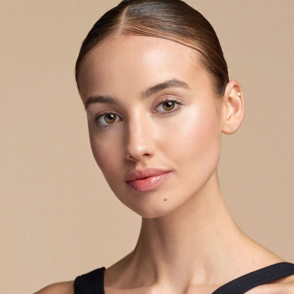 Porträt einer Frau mit glatter Haut und dezentem Make-up. Goldfarbener Schimmer auf den Wangen.