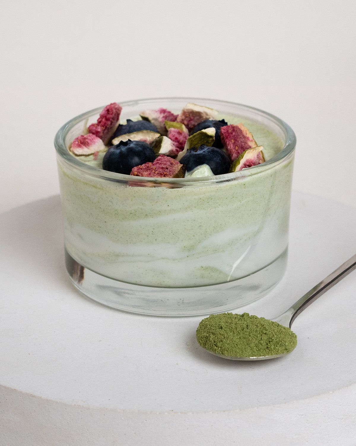 Glas mit grünem Inhalt, belegt mit Blaubeeren und Feigenstücken. Löffel mit grünem Pulver daneben.