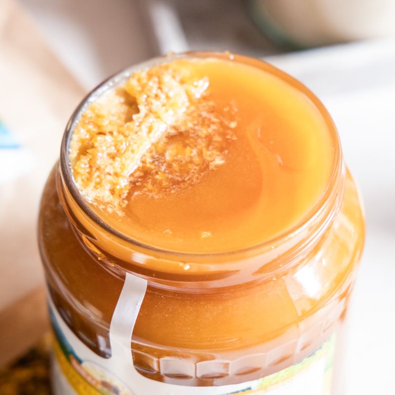 Nahaufnahme von Honig im Glas. Etikett teilweise sichtbar. Goldfarbener Deckel.
