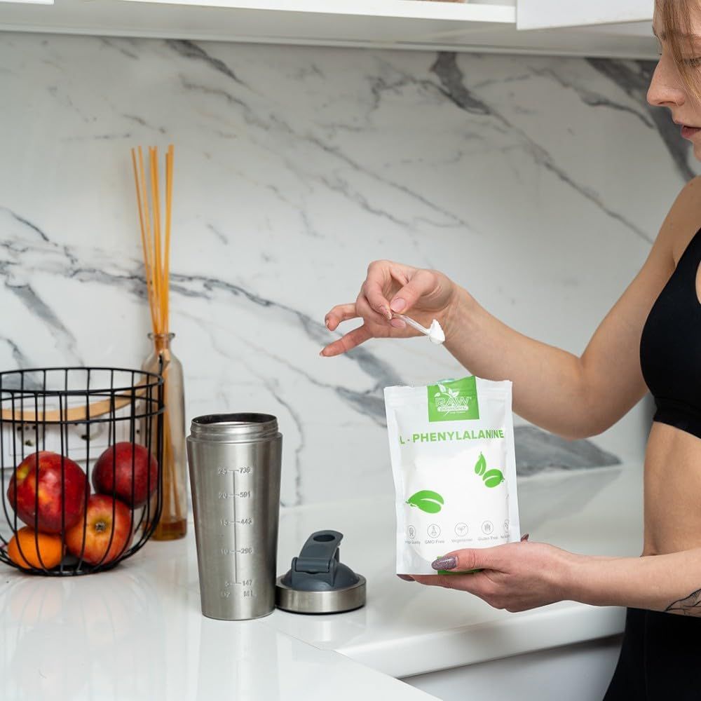 Eine Frau hält eine Packung L-Phenylalanin-Pulver. Daneben steht ein Shaker.