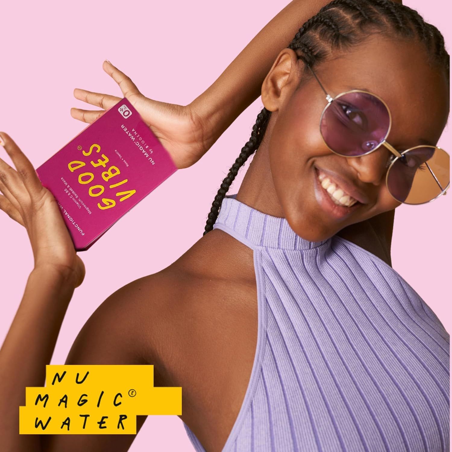 Person hält eine Packung Nu Magic Water. Aufschrift: GOOD VIBES, NU MAGIC WATER by BIOGENA. Rosa Verpackung, gelber Hintergrund.