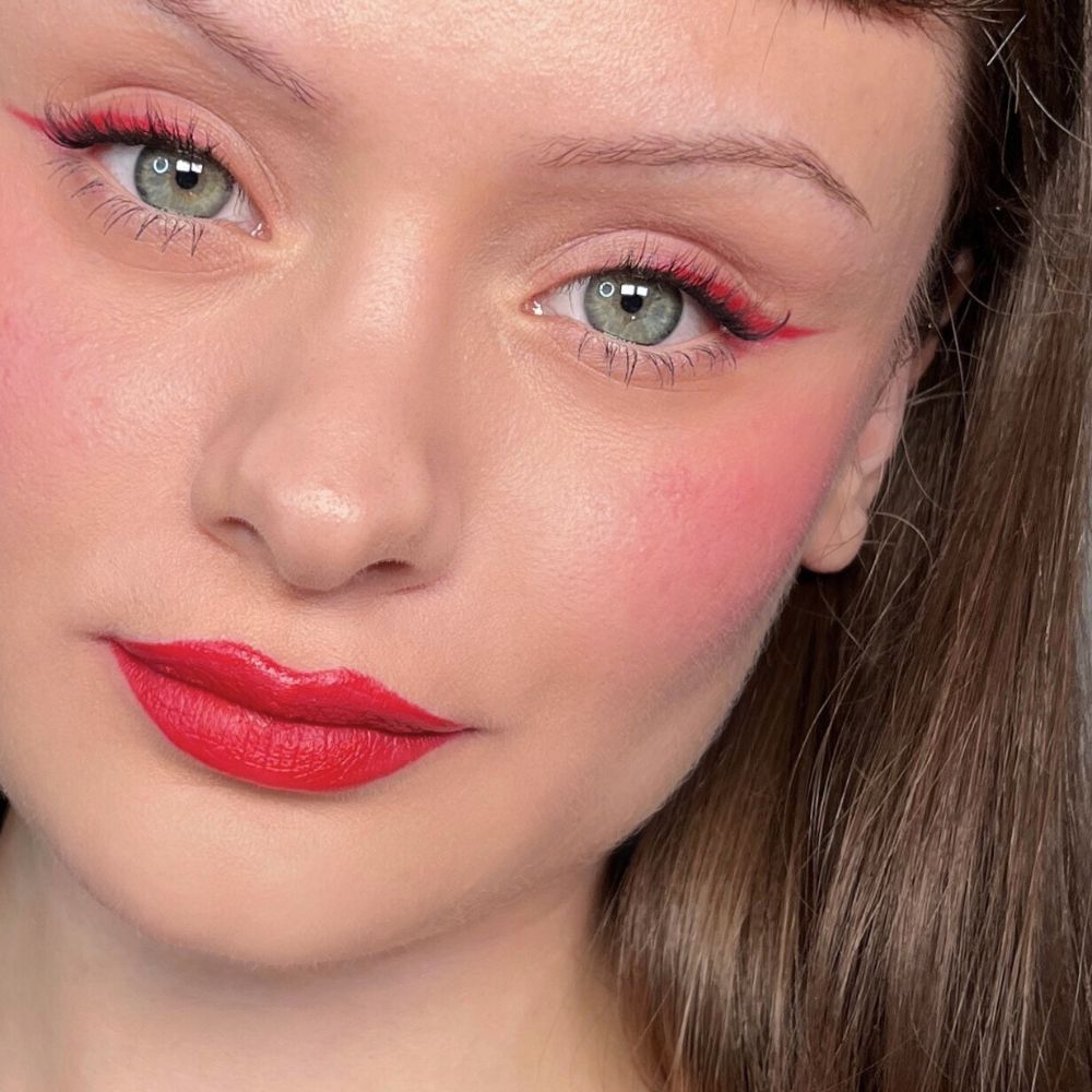 Nahaufnahme eines Gesichts mit rotem Eyeliner, Rouge und Lippenstift. Grüne Augen. Produkt: ALL TIGERS.