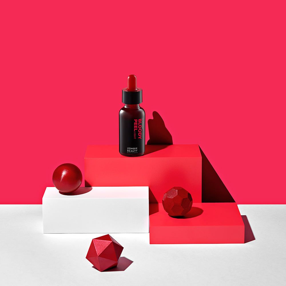 Produkt auf Podesten. Flasche mit roter Flüssigkeit, Kugeln und geometrischen Formen. Roter Hintergrund.
