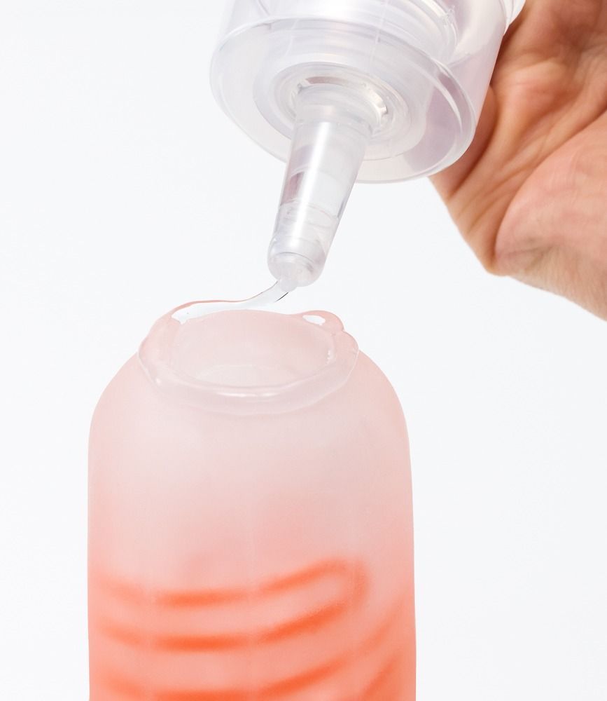 Flüssigkeit tropft aus einer Flasche in ein Objekt. Objekt hat eine rote Innenseite.