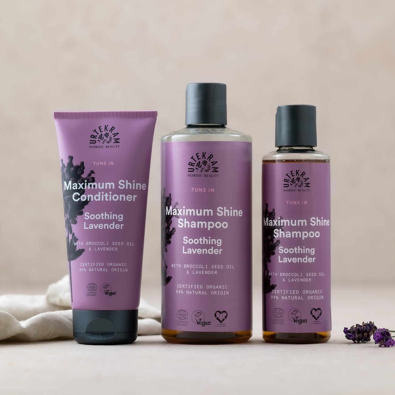 Drei Urtekram-Produkte: Conditioner, Shampoo (2x). Lila Etiketten, schwarze Deckel. Text: Soothing Lavender, Maximum Shine.