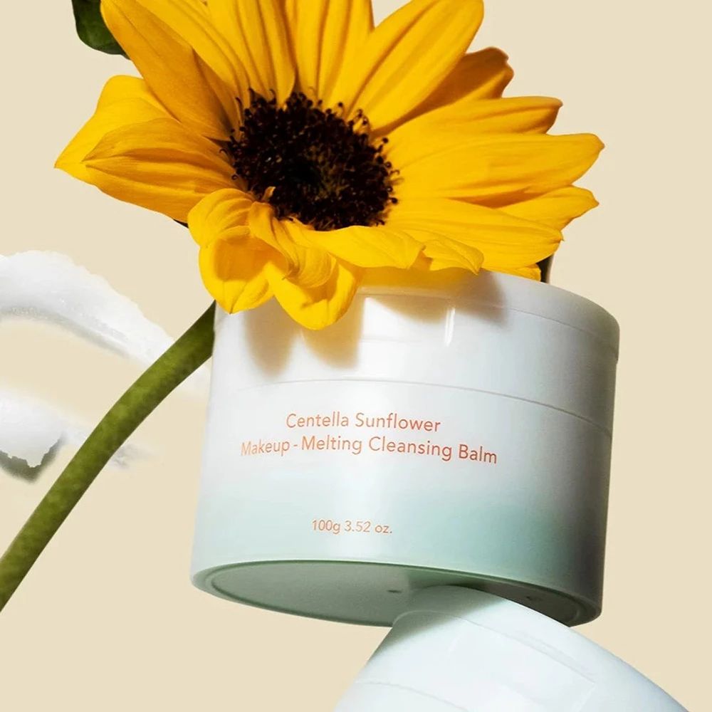 Weißer Tiegel mit Centella Sunflower Make-up-Schmelz-Reinigungsbalsam, 100g. Sonnenblume im Hintergrund.