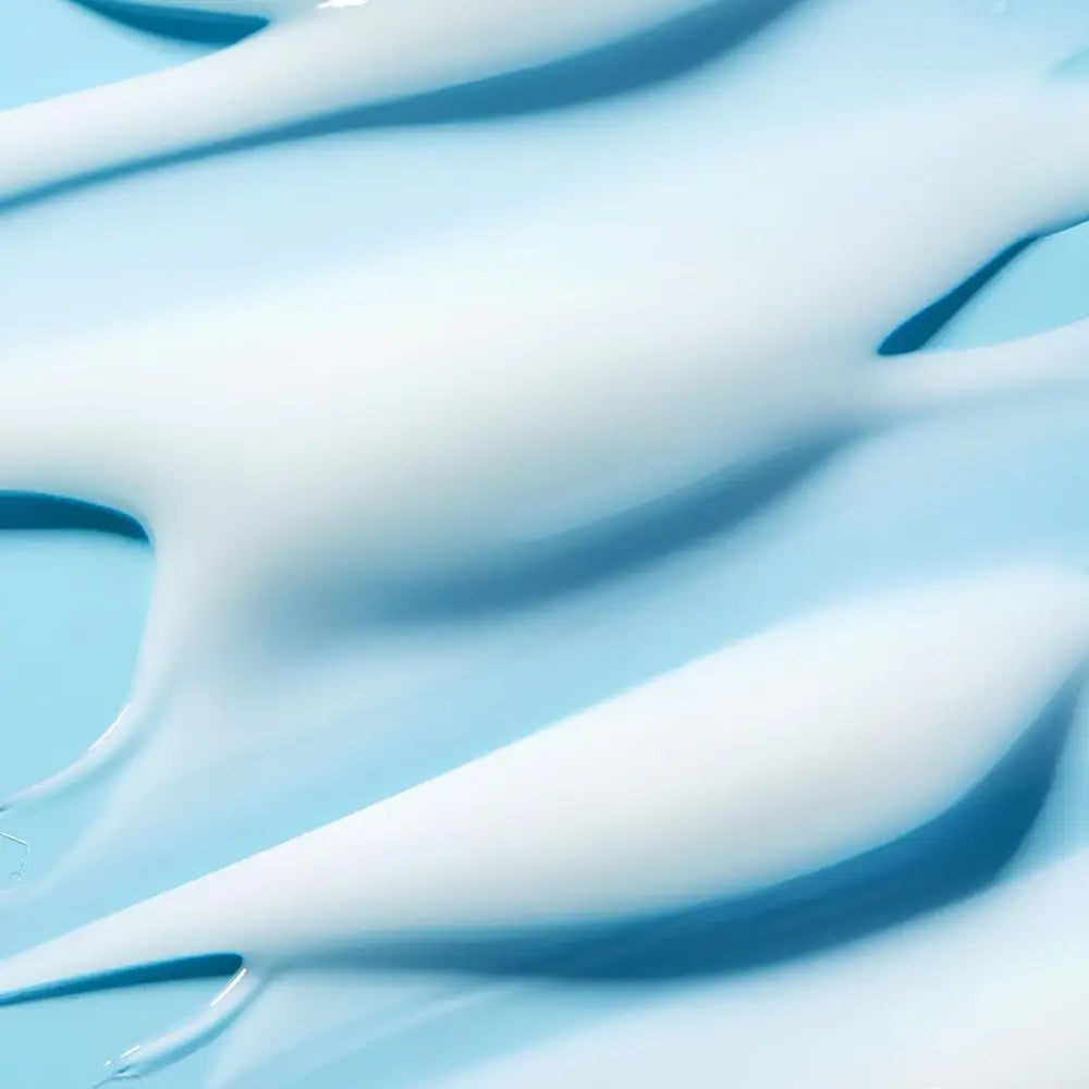 Nahaufnahme von weißen Creme-Schlieren auf hellblauem Hintergrund.